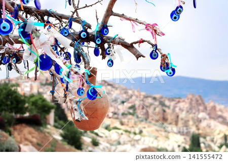 Traditional Turkish Nazar amulets, known as evil eye charms, hang in abundance from the branches of a wishing tree against the scenic backdrop of Pigeon Valley in Cappadocia, Anatolia, Turkey Traditional Turkish Nazar amulets, known as evil eye charms, hang in abundance from the branches of a wishing tree against the scenic backdrop of Pigeon Valley in Cappadocia, Anatolia, Turkey 141555472