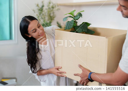 Happy Indian woman helping carry cardboard box with plant during home relocation Happy Indian woman helping carry cardboard box with plant during home relocation 141555516