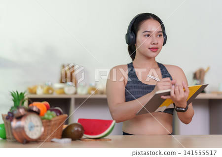 Young Asian woman wearing sportswear writing in notebook for healthy eating and wellness planning Young Asian woman wearing sportswear writing in notebook for healthy eating and wellness planning 141555517