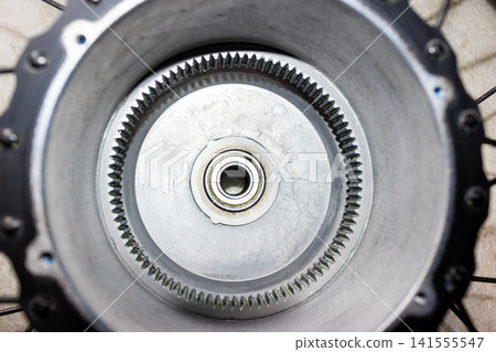Close-up view of an e-bike geared hub motor casing featuring a central ball bearing and an internal ring gear mechanism for electric bicycle propulsion systems, industrial machinery detail Close-up view of an e-bike geared hub motor casing featuring a central ball bearing and an internal ring gear mechanism for electric bicycle propulsion systems, industrial machinery detail 141555547