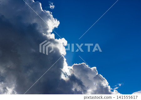 Dramatic sun rays breaking through heavy fluffy storm clouds, creating a vibrant contrast against the deep blue sky, perfect for nature concepts and meteorological backgrounds Dramatic sun rays breaking through heavy fluffy storm clouds, creating a vibrant contrast against the deep blue sky, perfect for nature concepts and meteorological backgrounds 141555617