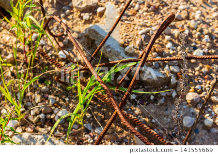 Rusty metal rebar protruding from abandoned concrete slab fragments on a gravel ground, discarded construction waste in a wasteland setting for scrap metal recycling Rusty metal rebar protruding from abandoned concrete slab fragments on a gravel ground, discarded construction waste in a wasteland setting for scrap metal recycling 141555669