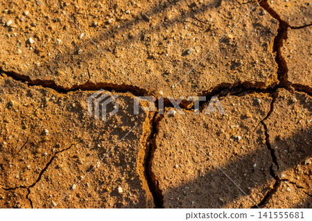 Severe drought causing deep cracks in parched clay soil, arid wasteland texture with scorched earth and natural patterns under bright sunlight showing environmental ecological damage Severe drought causing deep cracks in parched clay soil, arid wasteland texture with scorched earth and natural patterns under bright sunlight showing environmental ecological damage 141555681