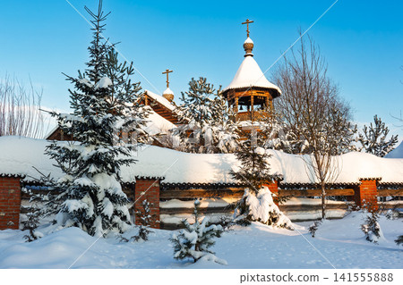 Stunning wooden Orthodox church nestled in deep snow under a clear bright winter sky, featuring a carved bell tower and evergreen trees covered in fresh powder, Russia Stunning wooden Orthodox church nestled in deep snow under a clear bright winter sky, featuring a carved bell tower and evergreen trees covered in fresh powder, Russia 141555888