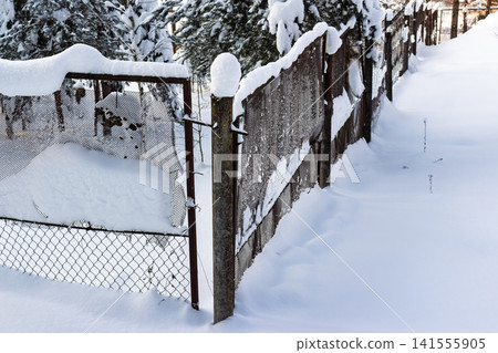 Rusted old boundary fence partially obscured by thick white snowdrifts in a winter forest scene Rusted old boundary fence partially obscured by thick white snowdrifts in a winter forest scene 141555905