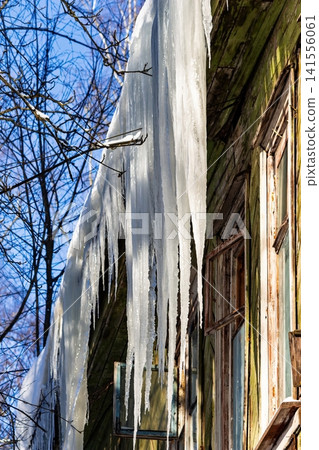 Massive, perilous icicles cling to a dilapidated wooden building, highlighting winter's raw power and potential hazard under a crisp sky Massive, perilous icicles cling to a dilapidated wooden building, highlighting winter's raw power and potential hazard under a crisp sky 141556061