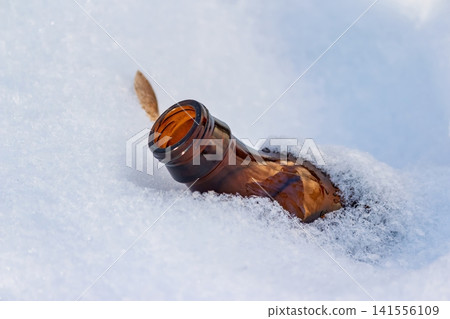 Abandoned brown beer bottle nestled in crisp white snow. A stark reminder of pollution amidst winter's serene, frozen landscape Abandoned brown beer bottle nestled in crisp white snow. A stark reminder of pollution amidst winter's serene, frozen landscape 141556109