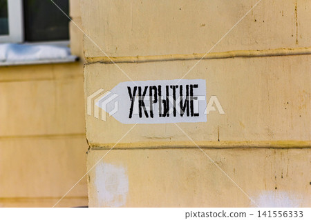 Russian SHELTER sign, a stark warning on a weathered building. Directing urban citizens to safety during ongoing conflict, Russia 141556333