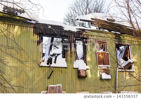 Abandoned wooden house, charred by fire, stands starkly in winter. Snow covers the burnt ruins, revealing a scene of profound devastation Abandoned wooden house, charred by fire, stands starkly in winter. Snow covers the burnt ruins, revealing a scene of profound devastation 141556337