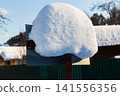 Winter's pristine snowdrift gently caps a rustic signpost against a clear blue sky, evoking serene rural charm in a frosty landscape 141556356