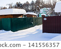 Charming snow-dusted village scene. Fresh white blankets cover rooftops and ground. Winter's serene embrace on a quiet rural street under blue sky 141556357