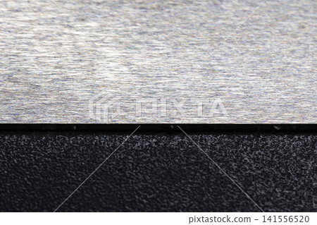 Closeup of a brushed metal plate above a rough textured black surface Closeup of a brushed metal plate above a rough textured black surface 141556520