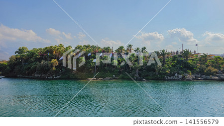 Lush tropical coastline with palm trees and waving national Greek flags along clear turquoise sea in Crete Greece for summer travel and vacation video background Lush tropical coastline with palm trees and waving national Greek flags along clear turquoise sea in Crete Greece for summer travel and vacation video background 141556579