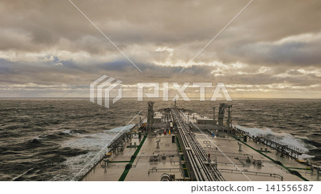 High angle view of large oil chemical tanker ship deck sailing through rough ocean water under dramatic cloudy sky at sunset for maritime industry background High angle view of large oil chemical tanker ship deck sailing through rough ocean water under dramatic cloudy sky at sunset for maritime industry background 141556587