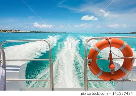 Boat wake across crystal clear tropical lagoon near luxury overwater resort villas Boat wake across crystal clear tropical lagoon near luxury overwater resort villas 141557454