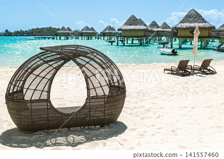 Wicker beach cabana overlooking turquoise lagoon and overwater resort villas Wicker beach cabana overlooking turquoise lagoon and overwater resort villas 141557460