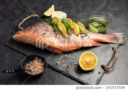 Freshly marinated raw Red snapper fish with lemon slices, garlic and rosemary herbs, on dark background Freshly marinated raw Red snapper fish with lemon slices, garlic and rosemary herbs, on dark background 141557504