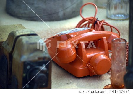 Retro orange vintage landline telephone displayed for sale at an outdoor flea market or garage sale, highlighting nostalgic communication technology. Retro orange vintage landline telephone displayed for sale at an outdoor flea market or garage sale, highlighting nostalgic communication technology. 141557655