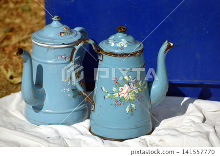 Two old blue enamel kettles decorated with floral patterns and light rust displayed for sale at an outdoor flea market Two old blue enamel kettles decorated with floral patterns and light rust displayed for sale at an outdoor flea market 141557770