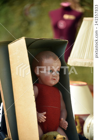 Beautiful vintage porcelain baby doll displayed among old objects at a flea market, showing a nostalgic atmosphere with antique treasures and childhood memories. Beautiful vintage porcelain baby doll displayed among old objects at a flea market, showing a nostalgic atmosphere with antique treasures and childhood memories. 141557833