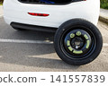 a temporary spare wheel resting on the car, ready to be changed 141557839
