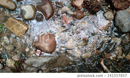 Clear stream water flowing over smooth stones and pebbles in natural setting Clear stream water flowing over smooth stones and pebbles in natural setting 141557857