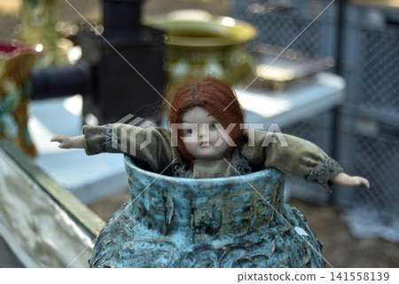 Beautiful retro porcelain doll displayed among vintage objects at a flea market, capturing a nostalgic atmosphere with antique decoration and childhood memories. 141558139