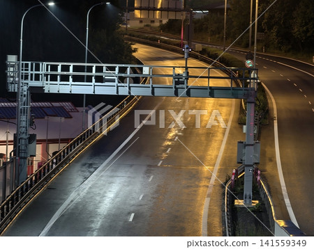 Empty wet highway at night with overhead gantry and streetlights Empty wet highway at night with overhead gantry and streetlights 141559349