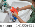 Young boy playing with a bright orange water gun at a bathroom sink 141559431
