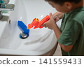 Child Aiming Water Gun at Sink, Engaging in Playful Activity 141559433