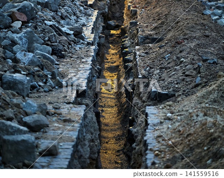 Sunlit narrow trench between stone rubble and excavated soil at construction site Sunlit narrow trench between stone rubble and excavated soil at construction site 141559516