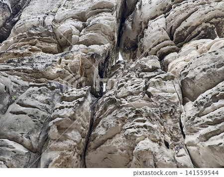 Weathered limestone cliff face with deep fissures and textured erosion Weathered limestone cliff face with deep fissures and textured erosion 141559544