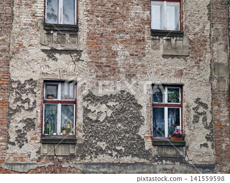 Weathered brick apartment facade with peeling plaster and four windows Weathered brick apartment facade with peeling plaster and four windows 141559598