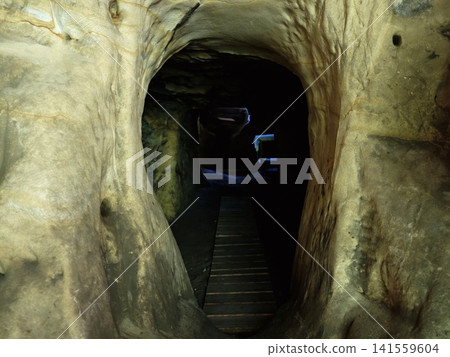 Narrow passageway through limestone cave with wooden walkway into darkness Narrow passageway through limestone cave with wooden walkway into darkness 141559604