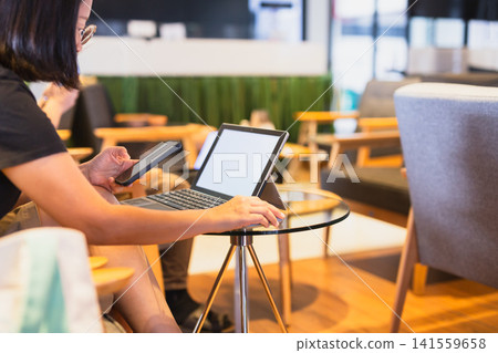 Woman using smartphone while working on laptop in co working space. Woman using smartphone while working on laptop in co working space. 141559658