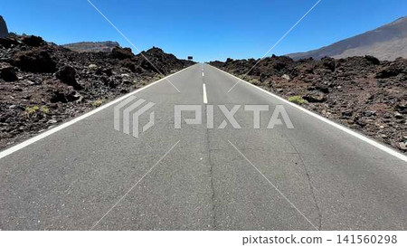 A breathtaking scenic road leads you through a stunning volcanic landscape beneath a clear blue sky A breathtaking scenic road leads you through a stunning volcanic landscape beneath a clear blue sky 141560298