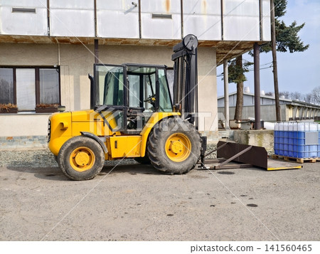 Yellow forklift stands idle outside factory. Loading bay forklift with crates in industrial yard Yellow forklift stands idle outside factory. Loading bay forklift with crates in industrial yard 141560465