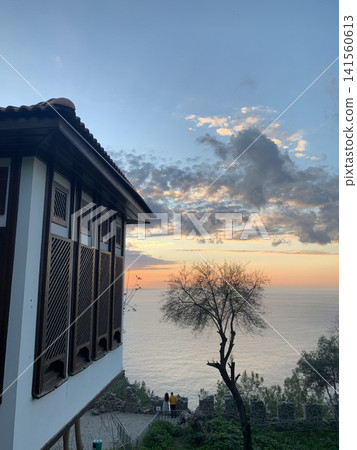 Sunset view over the ocean with tree silhouette and traditional architecture in foreground Sunset view over the ocean with tree silhouette and traditional architecture in foreground 141560613