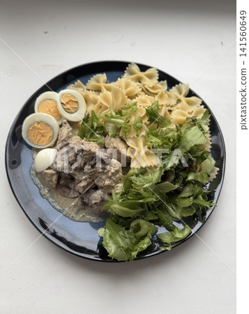 Plate of pasta, salad, and sliced boiled eggs on a black dish Plate of pasta, salad, and sliced boiled eggs on a black dish 141560649
