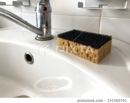 Kitchen sink with chrome faucet and sponge on white countertop 141560791