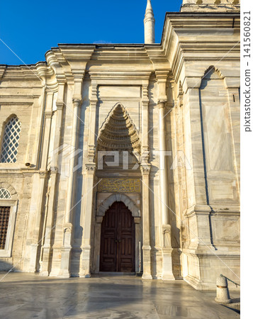 Ornate stone entrance of historical mosque with intricate architectural details and wooden door under clear blue sky Ornate stone entrance of historical mosque with intricate architectural details and wooden door under clear blue sky 141560821