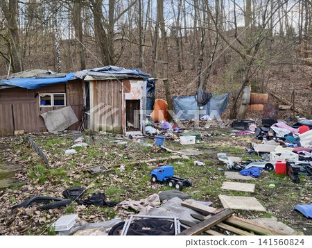 Abandoned forest shelter with debris. Neglected woodland site with discarded items and faded coverings Abandoned forest shelter with debris. Neglected woodland site with discarded items and faded coverings 141560824