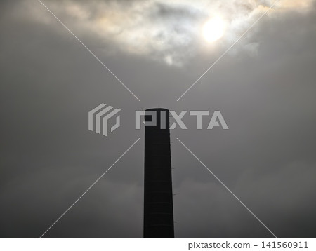 Silent smokestack scene. Isolated factory exhaust tower amid dark clouds and moody atmospheric shadows Silent smokestack scene. Isolated factory exhaust tower amid dark clouds and moody atmospheric shadows 141560911