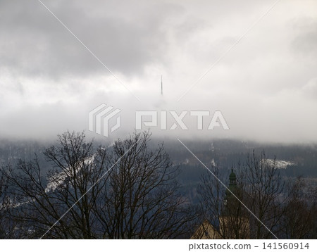 Hazy mountain peaks with surrounding trees. Serene mountain encased in fog with isolated trees nearby Hazy mountain peaks with surrounding trees. Serene mountain encased in fog with isolated trees nearby 141560914