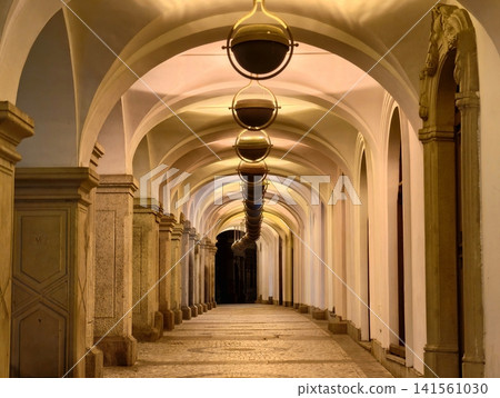 Elegant old hallway. Historic arched corridor adorned with glowing lamps and polished stone surface Elegant old hallway. Historic arched corridor adorned with glowing lamps and polished stone surface 141561030