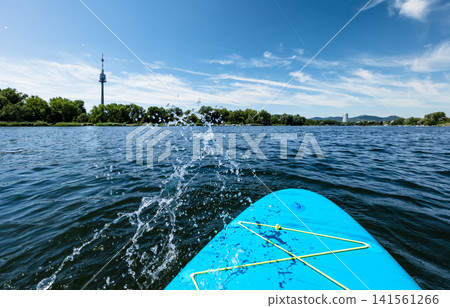 First person view from a stand up paddleboard on a river with a water splash, illustrating a dynamic summer water sport experience 141561266