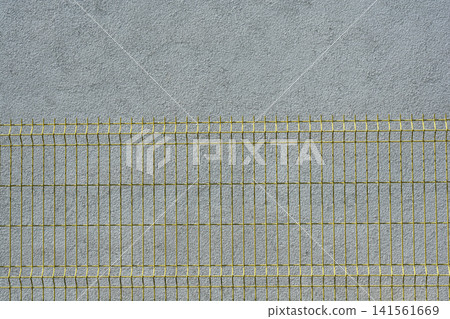 Yellow wire mesh fence panel against a grey plaster wall Yellow wire mesh fence panel against a grey plaster wall 141561669