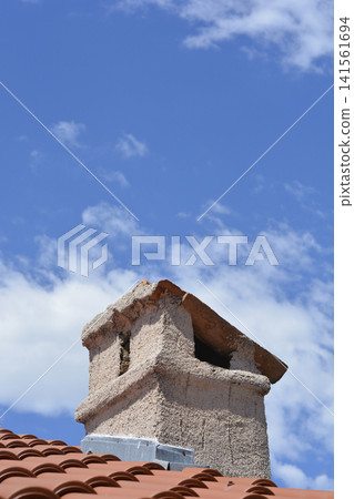 Traditional stone chimney on a roof against a blue sky with clouds. Traditional stone chimney on a roof against a blue sky with clouds. 141561694