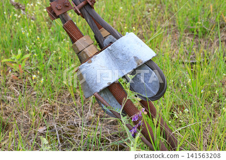 Guy-wire anchor system for securely anchoring a power line pole. Heavy steel cables and a rusty tensioning mechanism with a turnbuckle are anchored to the ground Guy-wire anchor system for securely anchoring a power line pole. Heavy steel cables and a rusty tensioning mechanism with a turnbuckle are anchored to the ground 141563208