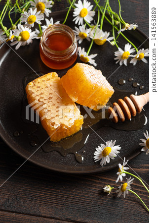 Golden honeycomb on black plate with chamomile flowers, fresh honey Golden honeycomb on black plate with chamomile flowers, fresh honey 141563889